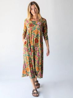 a woman standing in front of a white background wearing a dress with flowers on it