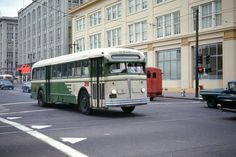 a green and white bus driving down a street next to tall buildings in the city