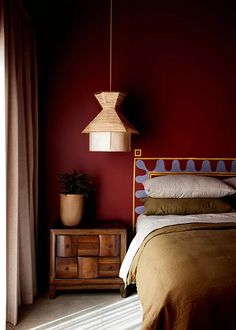 a bed sitting next to a wooden dresser under a light fixture in a room with red walls