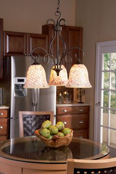 a chandelier hanging over a kitchen table with fruit on it in front of a refrigerator