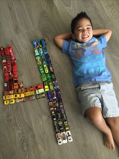 a young boy laying on the floor next to a letter made out of cars