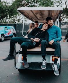 two men and a woman sitting on a golf cart in a parking lot with other people