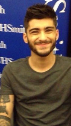 a man with tattoos standing in front of a blue sign and smiling at the camera