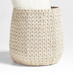 a white basket with a blanket on top and a pillow in the bottom that is made out of woven material