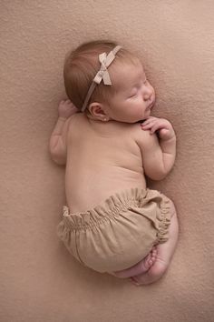 a baby laying on its side wearing a brown diaper and a bow in her hair