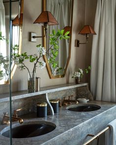 a bathroom with two sinks, mirrors and flowers in vases on the counter top