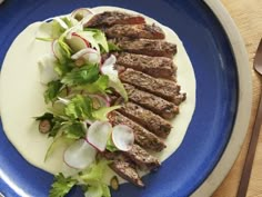 a blue plate topped with meat and veggies on top of a wooden table