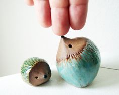 a hand reaching for a ceramic figurine next to an acorn on a white surface