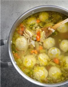 a pot filled with soup and dumplings on top of a table next to a wooden spoon