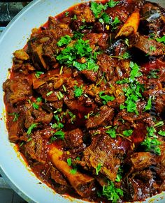 a white plate topped with meat covered in sauce and garnished with parsley