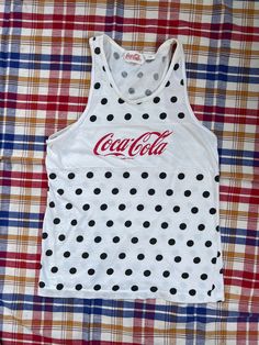 "Very cute vintage Coca-Cola tank top!  Very lightweight and soft 100% cotton, white with black polka dots and red lettering.  There are a few stains, 1 small pin prick on the front plus 1 other towards the side, and 2 towards the bottom on the back, but they are faint and honestly hard to see unless you are looking (see photos).   Tag says size large, though it seems to fit more of a modern woman's small or possibly medium.  Please check measurements to ensure a proper fit: Armpit to armpit (at tips/in line with tops of lower-case letters on graphic): 17\" Length from top of shoulder to bottom of shirt: 24\" Thanks for looking!  Check my shop for more vintage. Items will be shipped in reused packaging." Retro White Tank Top For Streetwear, White 90s Tank Top For Streetwear, 90s White Tank Top For Streetwear, 90s Style White Tank Top For Streetwear, Y2k Cotton Racerback Tank Top, Y2k Style Cotton Racerback Tank Top, White Y2k Cotton Tank Top, White Cotton Y2k Tank Top, White Cotton Y2k Style Tank Top