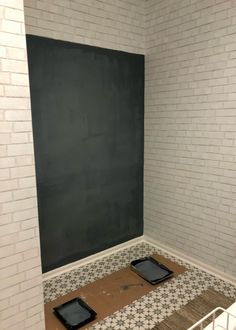 an empty room with two black trays on the floor and a chalkboard in the corner