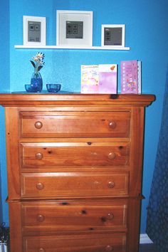 a wooden dresser in a blue room with pictures on the wall