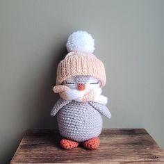 a crocheted penguin wearing a knitted hat and scarf on top of a wooden table