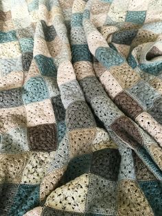 a crocheted blanket is laying on top of a bed with blue and brown colors