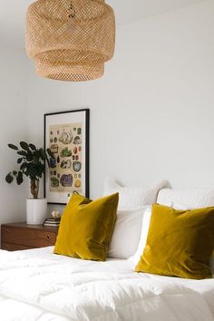 a bed with white sheets and yellow pillows in a small room next to a potted plant