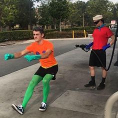 a man in an orange shirt and black shorts kicking a soccer ball on the street