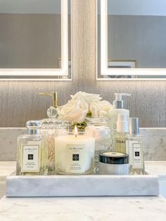 a bathroom counter with candles, soaps and other items on it in front of two mirrors