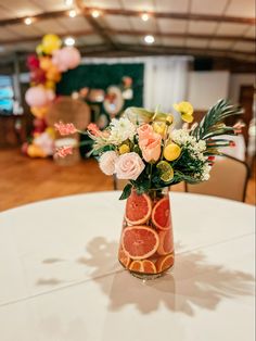 a vase filled with flowers and fruit sitting on top of a white table covered in balloons