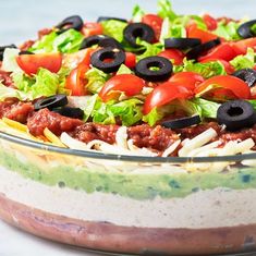 a layered salad with black olives, lettuce and tomatoes in a glass dish