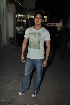 a man standing on the sidewalk at night with his hands in his pockets and looking into the camera