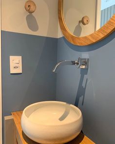 a bathroom sink sitting under a mirror next to a wall mounted faucet in front of a round mirror