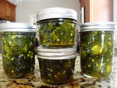 four jars filled with pickles sitting on top of a counter