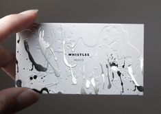 a person holding up a business card with black and white paint splattered on it