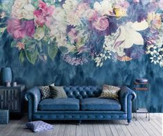 a blue couch sitting in front of a wall with flowers painted on it's side