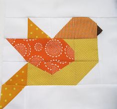 an orange and yellow bird is on top of a white piece of fabric that has been stitched together