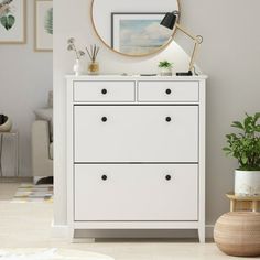 a white dresser with two drawers and a round mirror on the wall next to it