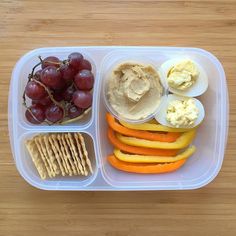 a plastic container filled with fruit, crackers and hummus next to some grapes