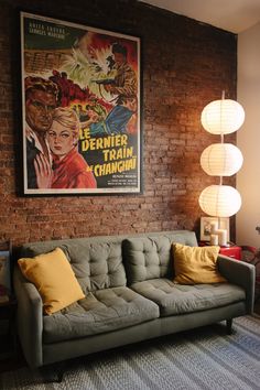 a grey couch sitting in front of a brick wall with two lamps on top of it