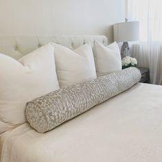 a bed with white pillows and a large pillow on it's headboard in front of a window