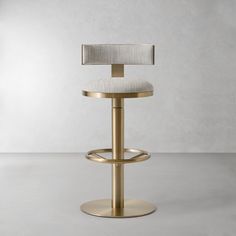 a gold stool with a white upholstered seat and back rests in front of a plain wall