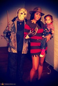 a woman holding a child and standing next to a man in a costume with a mask on