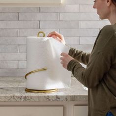 a woman holding a roll of toilet paper in front of a white counter top with a gold handle