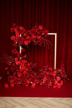 red flowers are arranged in the shape of a square frame on a wooden floor next to a red curtain