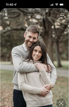 a man and woman hugging each other in front of trees