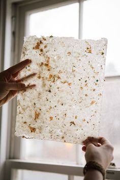 a person holding up a piece of food in front of a window with their hands