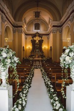 an aisle lined with white flowers and greenery in front of a church pews