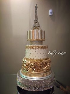 a three tiered cake is adorned with gold and silver decorations, including the eiffel tower