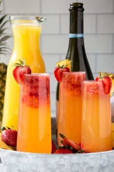 three glasses filled with orange juice and strawberries next to two bottles of champagne on a table