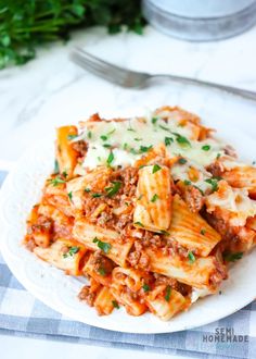 a white plate topped with pasta covered in sauce and parsley next to a fork