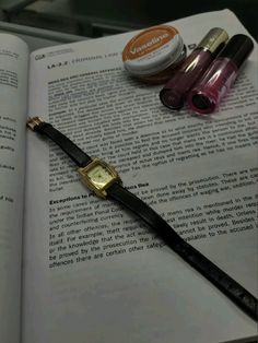 a watch sitting on top of an open book next to some nail polish and a pen