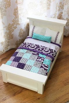 a doll bed with purple and blue quilted bedspread on top of it