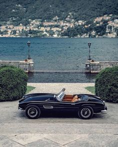 an old black convertible car parked in front of a lake