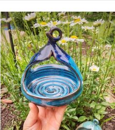 a hand holding up a blue glass bowl in front of some daisies and wildflowers