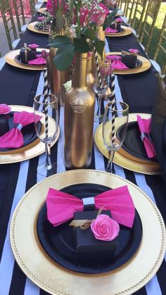 the table is set with black and gold plates, pink napkins, and silverware