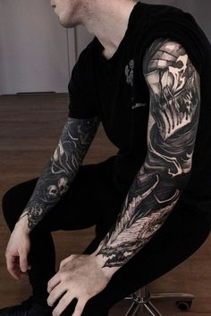 a man sitting on the floor with his arm covered in black and grey tattoos,